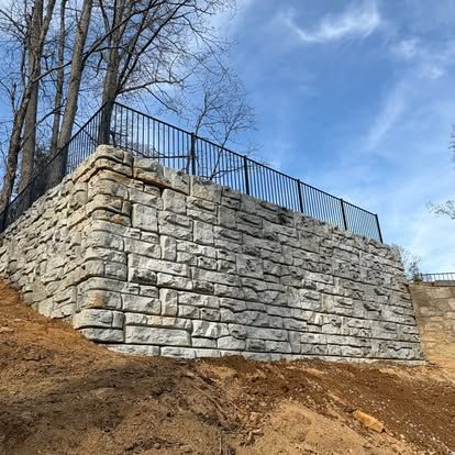 Tall stacked stone-block retaining wall with a black railing on top