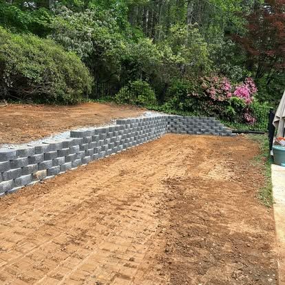 Curved block retaining wall with freshly graded soil and blooming shrubs