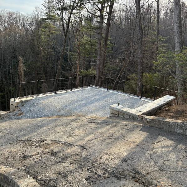 New gravel parking pad edged with a stone wall and railing in the woods